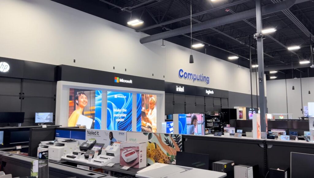 A spacious electronics store featuring numerous computers and monitors displayed on shelves and tables.